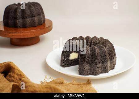 Nahaufnahme eines mit Käse gefüllten schwarzen klebrigen Reiskuchens, serviert auf einem weißen Teller. Ein klassisches indonesisches hausgemachtes Dessert mit weicher Textur Stockfoto