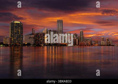 Dieser Blick auf die Skyline von Miami in der Abenddämmerung zeigt die leuchtenden Hochhäuser von Downtown und Brickell, die sich auf dem ruhigen Wasser der Biscayne Bay spiegeln. Stockfoto