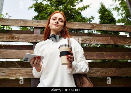 Eine junge Frau entspannt sich mit Kaffee und blättert auf ihrem Handy. Stockfoto