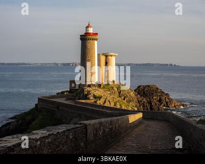 Der Leuchtturm Petit Minou, der zur goldenen Stunde in der Nähe von Brest, Bretagne, Frankreich gesehen wird, steht an der felsigen Küste und blickt im warmen Sonnenuntergang auf das Meer. Stockfoto