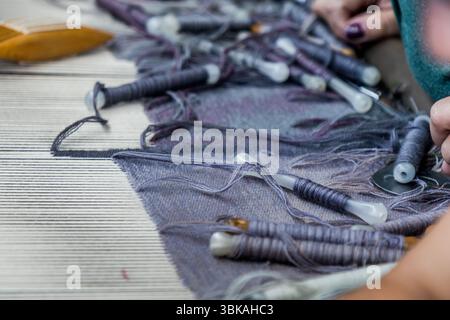 Atelier Robert Four in Aubusson, wo der Wandteppich Hommage à George Sand hergestellt wird. Nahaufnahme des Shuttles mit Wollgarn in verschiedenen Farben und ein Abschnitt der Kette, die straffen Längsfäden im Webstuhl, durch die das Shuttlegarn mit dem Schussfaden geführt wird. Rue Madeleine, Aubusson, Nouvelle-Aquitaine, Frankreich Stockfoto
