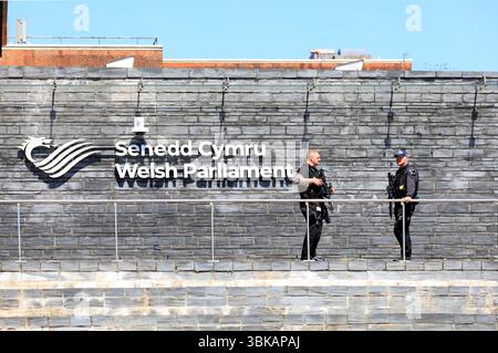 Bewaffnete Polizeibeamte aus Südwales / Heddlu - im Dienst vor dem walisischen Parlament / Senedd Gebäude, Cardiff Bay. Vom Mai 2025 im Frühjahr Stockfoto