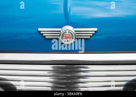 Nahaufnahme eines klassischen Mini Cooper geflügelten Chrom-Emblems mit dem Logo des Lorbeerkranzes auf der Motorhaube eines blauen Mini Cooper Stockfoto