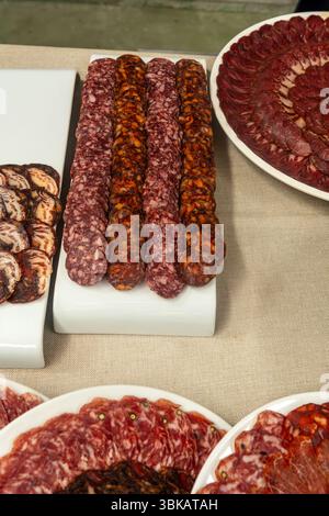 Auswahl an geschnittenem geräuchertem Fleisch, einschließlich Chorizo, Salchichon und Lomo auf weißen Tellern. Stockfoto