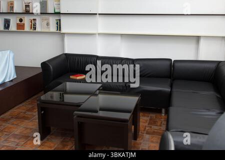 CHISINAU, MOLDAWIEN - 14. MÄRZ 2025; Schwarzes Ecksofa aus Leder mit Kaffeetischen aus Glas in einem gemütlichen Bibliotheksraum mit Büchern auf weißen Wandregalen, modern Stockfoto