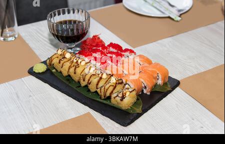 Sushi-Brötchen mit Lachs, Tobiko und Tempura auf Schieferplatte, realistischer Stil, auf weißem Holztisch, Konzept der japanischen Küche Stockfoto