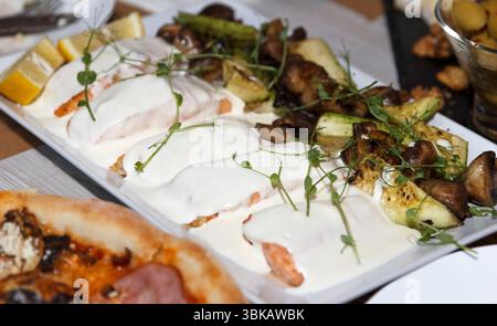 Gegrillte Lachsfilets mit weißer cremiger Sauce und Kräutern, serviert mit geröstetem Gemüse auf einem weißen Keramiktablett, Gourmet-Konzept Stockfoto