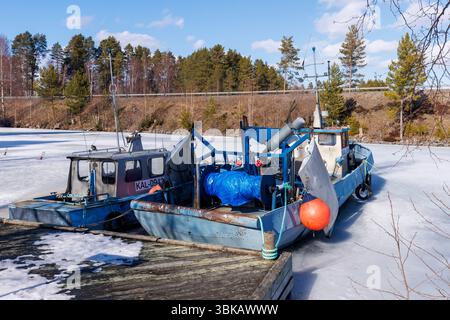 Kleine Binnenfischtrawler ankerten und stecken im Eis im Frühling am Jachthafen Kivisalmi, See Etelä-Konnevesi, Finnland Stockfoto