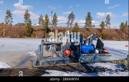 Kleine Binnenfischtrawler ankerten und stecken im Eis im Frühling am Jachthafen Kivisalmi, See Etelä-Konnevesi, Finnland Stockfoto