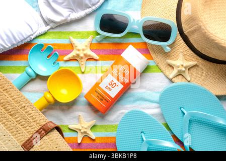 Blick von oben auf eine Flasche Sonnencreme mit 50+ Aufschriften, Sonnenbrillen und Strandartikel auf einem Strandtuch. Konzept des Sonnenschutzes Stockfoto