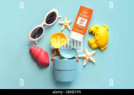 Blick von oben auf eine Flasche Sonnencreme mit 50+ Aufschriften, Sonnenbrille und Strandeimer über blauem Hintergrund. Konzept des Sonnenschutzes Stockfoto