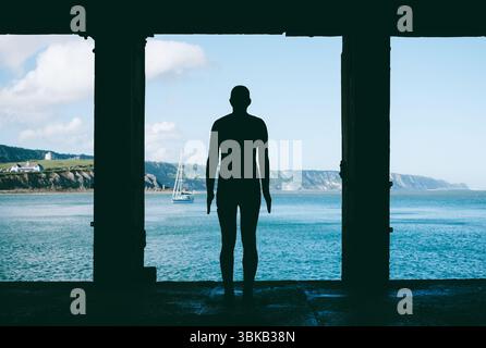Die Skulptur „Folkestone man“ oder „Another Time“ von Antony Gormley steht in einer Silhouette, perfekt eingerahmt von einer Öffnung mit Blick auf das blaue Meer. Stockfoto