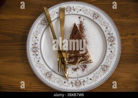 Dreieckiges Tiramisu mit Schokoladenchips auf einem runden Teller auf einem Tisch, Draufsicht Stockfoto
