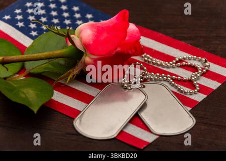 Nahaufnahme einer roten Rose und Armeehundmarken, die auf einer amerikanischen Flagge ruhen, symbolisieren Erinnerung und Respekt vor Veteranen und gefallenen Soldaten Stockfoto