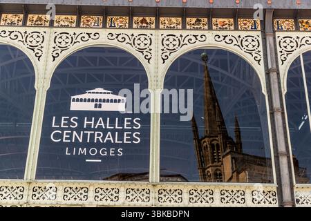 Ein gewölbtes Fenster der Markthalle (Halles centrales) auf dem Place Saint-Michel in Limoges, Haute-Vienne, Nouvelle-Aquitaine, Frankreich, spiegelt den Turm der Kathedrale wider (möglicherweise der Kirche Saint-Michel-des-Lions). Das Glas trägt die Aufschrift „Les Halles Centrales Limoges“ mit einer Zeichnung des Gebäudes. Über den Fenstern verläuft ein Fries aus Porzellanfliesen mit Tierköpfen, floralen Ranken und dem Buchstaben L. Die Markthalle wurde zwischen 1885 und 1889 nach Plänen der Architekten Pesce und Lévesque errichtet. Ursprünglich sollte sie sogar Gustave Eiffel bauen. Das 1.200 Quadratmeter große Innere ha Stockfoto