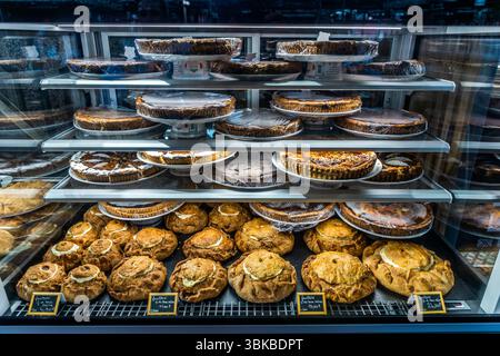Kartoffelkuchen (tourte, französisches Pâté de pommes de terre) liegen in einer Glasvitrine in der Markthalle (Halles centrales) auf dem Place de la Motte in Limoges, Haute-Vienne, Nouvelle-Aquitaine, Frankreich. Sie gehören zu den Spezialitäten der Stadt und des Limousin. Die herzhaften Blätterteigkuchen enthalten Kartoffeln, Crème fraîche und manchmal Fleisch. Sie liegen in verschiedenen Größen mit gefalteten, goldbraunen Rändern auf dem unteren Regal, und kleine Kreidetafeln zeigen die Preise. Runde Kuchen und Torten, einige in Folie eingewickelt, stehen auf den oberen Regalen. Die Markthalle wurde zwischen 1885 und 1889 nach Plänen des Architekten erbaut Stockfoto