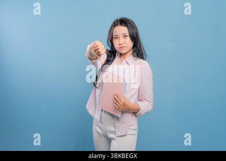 Eine Frau hält ein rosafarbenes Buch und gibt die Daumen nach unten. Begriff der Missbilligung oder Unzufriedenheit Stockfoto