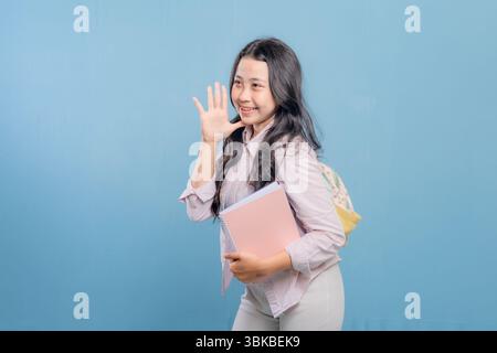 Eine Frau lächelt und winkt in die Kamera, während sie einen Stapel Bücher hält. Vorstellung von Glück und Aufregung, da die Frau stolz auf ihre Bücher ist oder Stockfoto