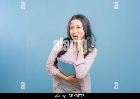 Eine Frau lächelt und winkt in die Kamera, während sie einen Stapel Bücher hält. Vorstellung von Glück und Aufregung, da die Frau stolz auf ihre Bücher ist oder Stockfoto