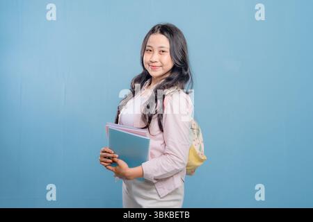 Eine Frau hält ein Buch und einen Rucksack in der Hand. Sie lächelt und sieht in die Kamera. Das Konzept von Selbstvertrauen und Bereitschaft, auf das die Frau vorbereitet ist Stockfoto