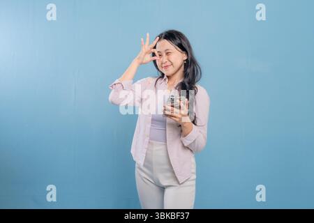 Eine Frau posiert für ein Foto mit erhobener Hand und hält ein Handy. Konzept moderner Technik und Kommunikation Stockfoto