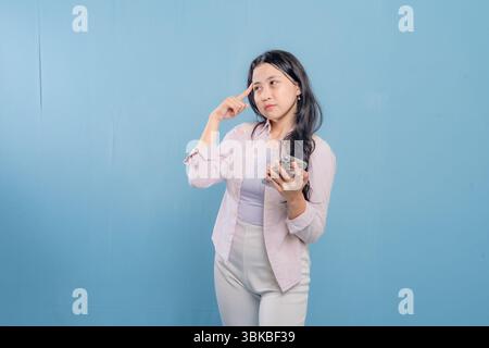 Eine Frau steht vor einer blauen Mauer, schaut nach unten und denkt. Sie trägt ein weißes Hemd und eine weiße Hose Stockfoto