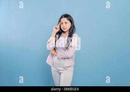 Eine Frau steht mit überkreuzten Armen vor einer blauen Wand. Sie blickt nach unten und ist tief in Gedanken Stockfoto