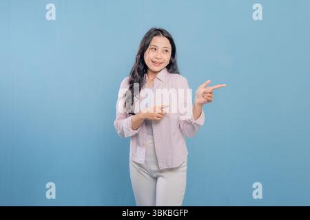 Eine Frau zeigt auf etwas, während sie ein rosa Hemd und eine weiße Hose trägt. Das Konzept der Neugier und des Interesses an dem Thema, auf das verwiesen wird Stockfoto