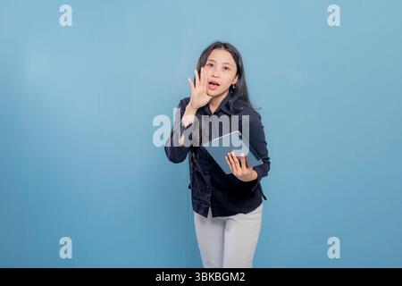 Eine Frau in einem schwarzen Hemd und einer weißen Hose hält eine Tablette in der Hand. Sie schaut in die Kamera und ist in einer ernsten oder fokussierten Stimmung Stockfoto