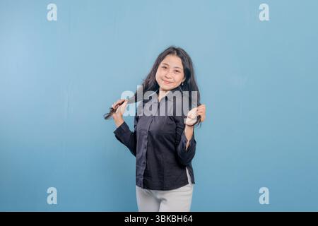 Eine Frau mit langen Haaren lächelt und hält ihre Haare zurück. Sie trägt ein schwarzes Hemd und eine weiße Hose Stockfoto