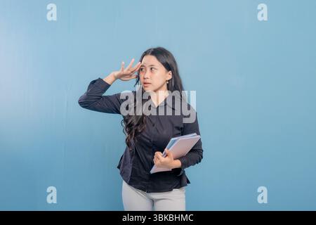 Eine Frau schaut in den Himmel, während sie ein Buch hält. Sie ist tief in Gedanken oder denkt über etwas nach Stockfoto