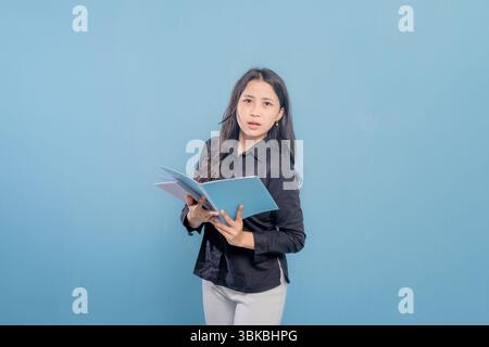Eine Frau liest ein Buch, während sie in die Kamera schaut. Sie ist überrascht oder schockiert von etwas, das sie liest Stockfoto