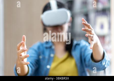 Eine junge Frau, die ein VR-Headset trägt, interagiert während des Studiums in einer Bibliothek mit virtuellen Inhalten und symbolisiert moderne Bildung und immersive Technologie. Stockfoto