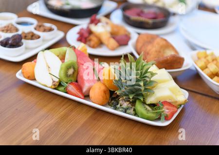Ein großer Teller mit frischem Obst mit getrockneten Früchten, Nüssen und Marmeladen auf einem Holztisch während eines Frühstückserlebnisses im Hotel. Stockfoto