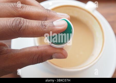 Junger Mann, der künstliche Süßstoffe in eine Tasse Tee auf dem Tisch steckt. Stockfoto