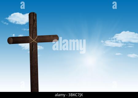 Das Holzkreuz mit flachem Design steht vor dem hellblauen Himmel mit Sonnenaufgang und verstreuten Wolken Stockfoto