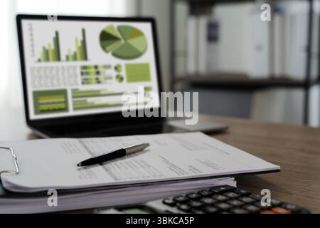 Eine umweltfreundliche Berichtsdatei zeigt einen Schreibtisch mit Finanzdokumenten, Stift und Laptop mit Diagrammen und Diagrammen, die Geschäfts- oder Finanzdaten anzeigen Stockfoto