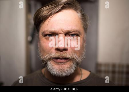 Ein Mann mit Gesichtsbehaarung, einschließlich Bart und Schnurrbart, schneidet sich die Stirn hoch und macht ein lustiges Gesicht, zeigt Falten und einen zufriedenen Ausdruck Stockfoto