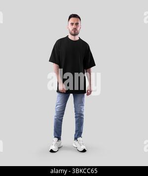 Modell eines schwarzen Oversize-T-Shirts auf bärtigem Mann in Jeans, Turnschuhen, durchgehende Vorderansicht, isoliert auf Hintergrund. Modische legere Faultvorlage Stockfoto