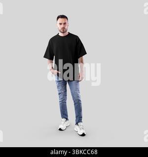 Modell eines schwarzen Oversize-T-Shirts auf bärtigem Kerl, Hand in Jeanstasche, Sneakers, durchgehende Vorderansicht, isoliert auf Hintergrund. Produktfotografie. Stockfoto