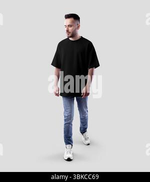 Modell eines schwarzen Oversize-T-Shirts auf einem bärtigen Walking Guy in Jeans, Sneakers, durchgehender Vorderansicht, Designbekleidung, Branding. Produktfoto Stockfoto
