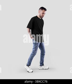 Modell eines schwarzen Oversize-T-Shirts auf einem bärtigen Walking Guy, Seitenansicht in voller Länge, Hände in Jeanstasche, Sneakers. Herrenbekleidung Vorlage, isoliert Stockfoto