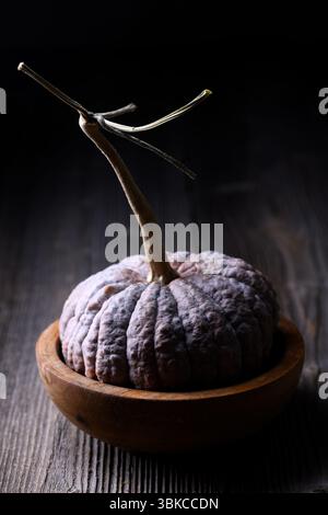 Schwarzer Futsu-Kürbis mit faltiger Haut liegt im engen Herbstrahmen auf einer Holzplatte auf. Saisonale Produktionsszene, perfekt für das Styling von Speisen und für die Ausstellung von Erbstücken Stockfoto