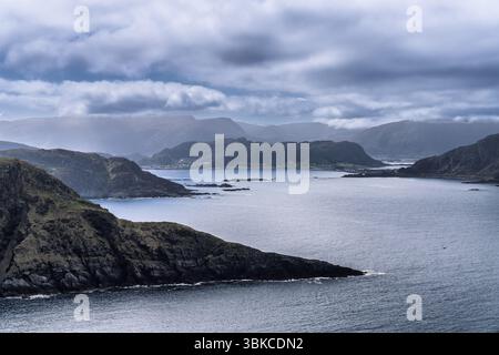 Atemberaubende Küstenlandschaft mit zerklüfteten Klippen, ruhigem Wasser und einer bergigen Kulisse unter einem bewölkten Himmel, die ein ruhiges und natürliches Atmo schafft Stockfoto