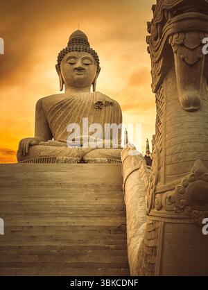 Weiße Buddha-Statue im goldenen Licht. Großes Buddha-Denkmal auf dem Gipfel des Berges von Phuket, Thailand. Touristenziel und Ort der buddhistischen Anbetung. Reiseziel für Touristen. Orangentonfilter Stockfoto