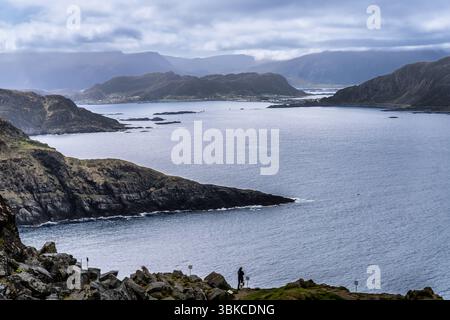Atemberaubende Küstenlandschaft mit zerklüfteten Klippen, ruhigem Wasser und einer bergigen Kulisse unter einem bewölkten Himmel, die ein ruhiges und natürliches Atmo schafft Stockfoto