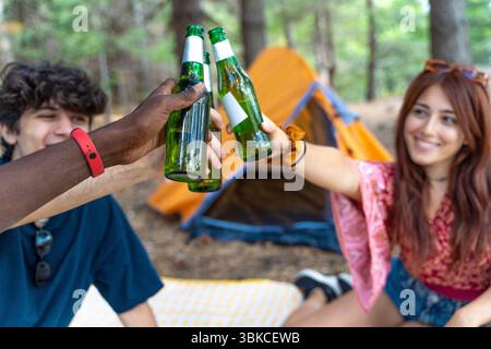 Ein aus der Perspektive einer Gruppe verschiedener Freunde, die bei einer Feier während eines Campingausflugs mit Bierflaschen getoastet haben Stockfoto