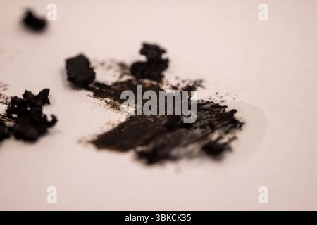 Abstraktes Nahbild eines schwarzen Holzkohle-Flusses auf weißem Papier, mit verstreuten Fragmenten und Pudertextur, die ein ausdrucksstarkes künstlerisches Bild schaffen. Stockfoto