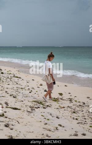 Frau, die allein an einem bewölkten Tag am tropischen Strand spaziert Stockfoto