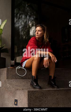 Nachdenkliche junge Frau, die vor dem Café mit Kaffee und Zigarette sitzt Stockfoto